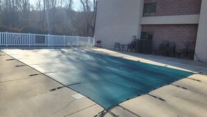An outdoor pool area with a white fence, chairs, and a brick building in the background.