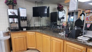 A kitchen area with a coffee machine, a waffle maker, and a sign indicating no breakfast outside.