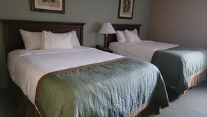 Two single beds with wooden headboards, white bedding, and green throw blankets. There are framed botanical prints on the walls.
