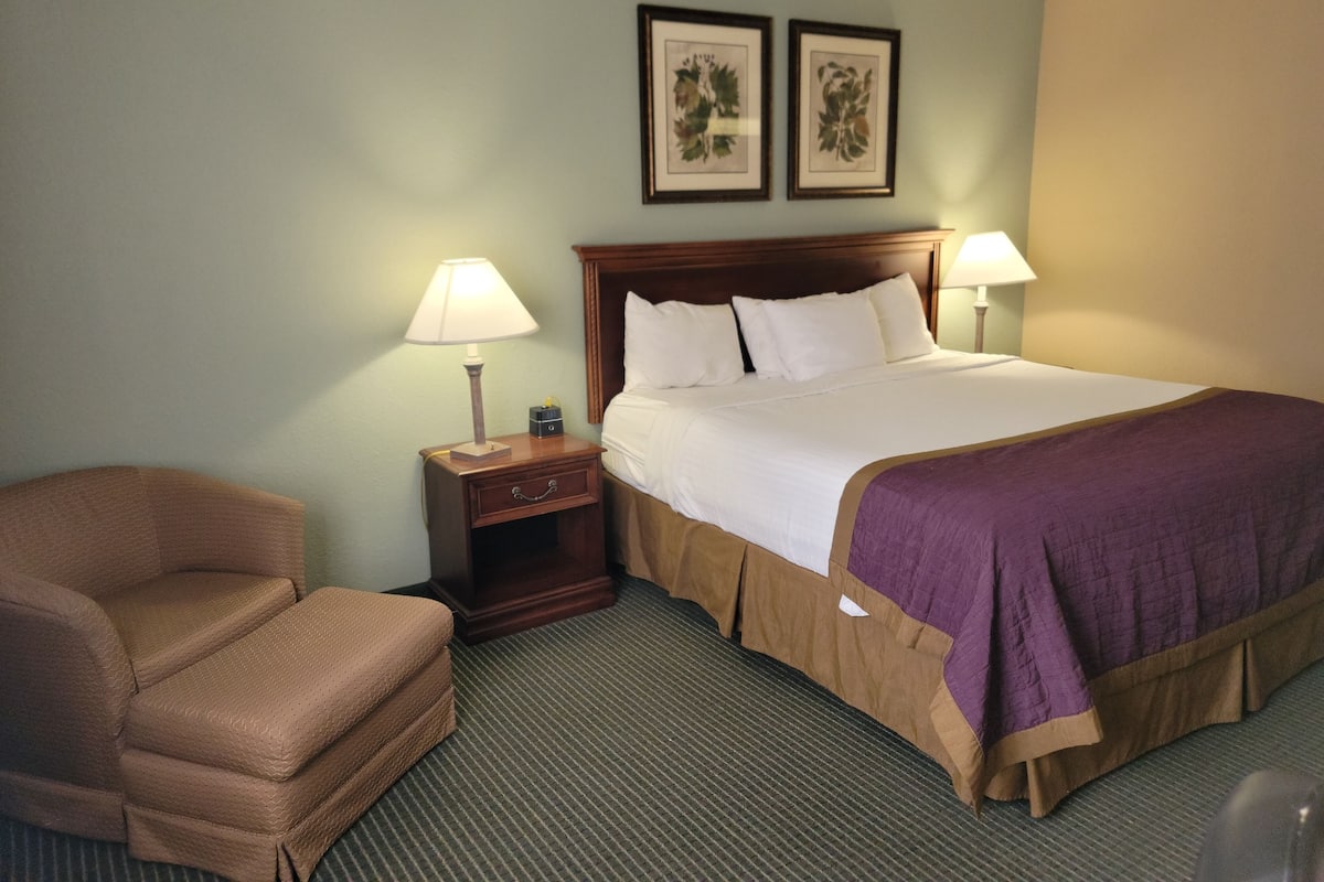 A hotel room with a bed, two bedside lamps, a nightstand, a chair, and two framed pictures on the wall.