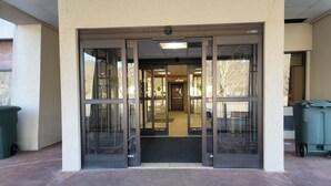 A building entrance with glass doors, a visible interior hallway, and a trash bin outside.