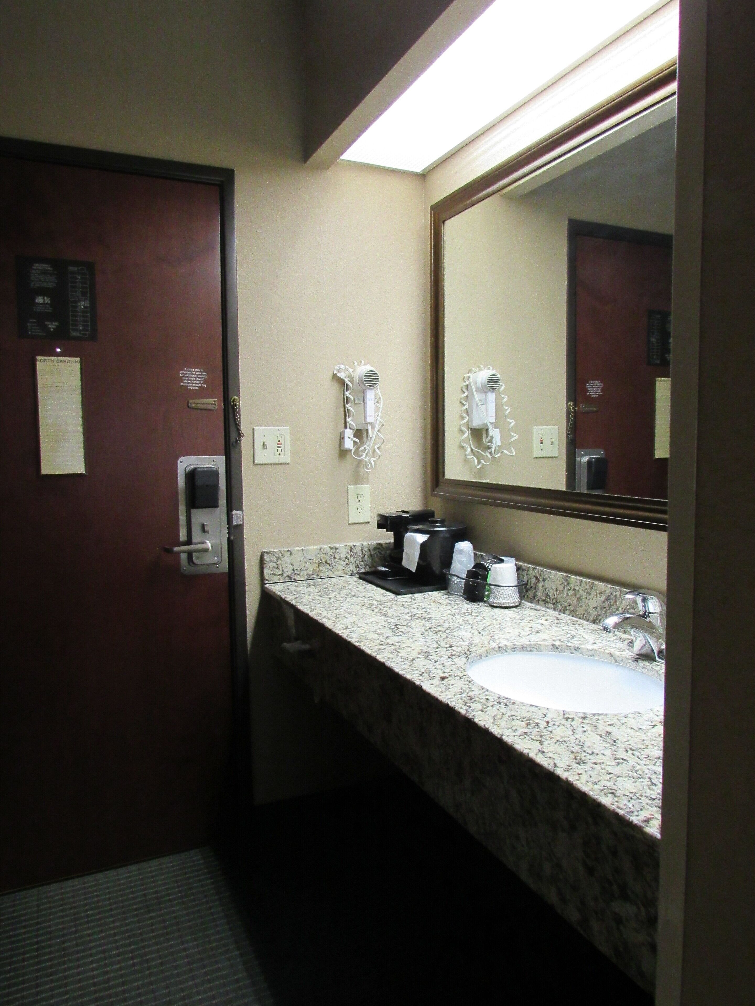 A bathroom with a marble sink, a mirror, a hairdryer, and a coffee maker.
