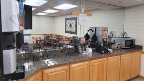 A kitchen area with a coffee machine, toaster, waffle maker, and microwave. There is a sign on the wall and a framed picture above the counter.
