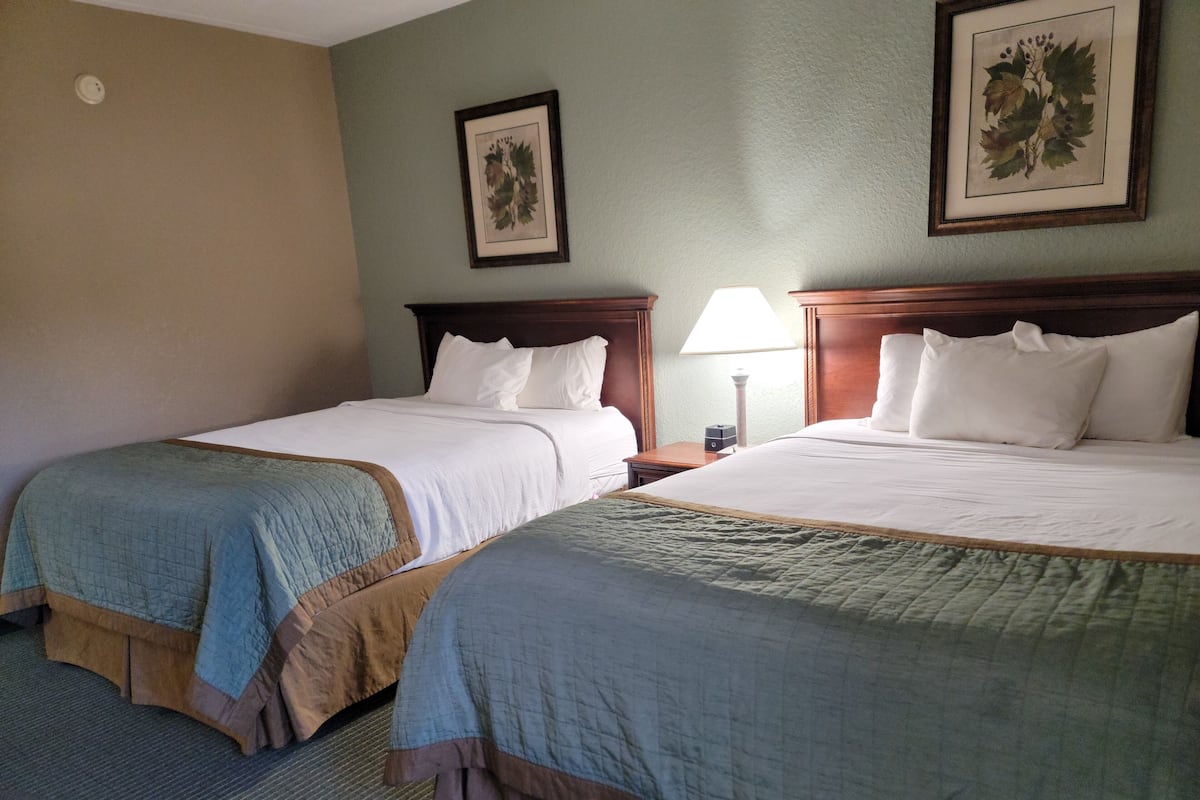 Two double beds with headboards, a nightstand with a lamp, and a framed botanical print on the wall.