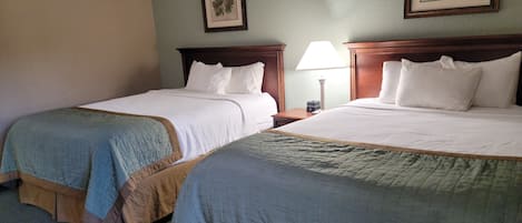 Two double beds with headboards, a nightstand with a lamp, and a framed botanical print on the wall.
