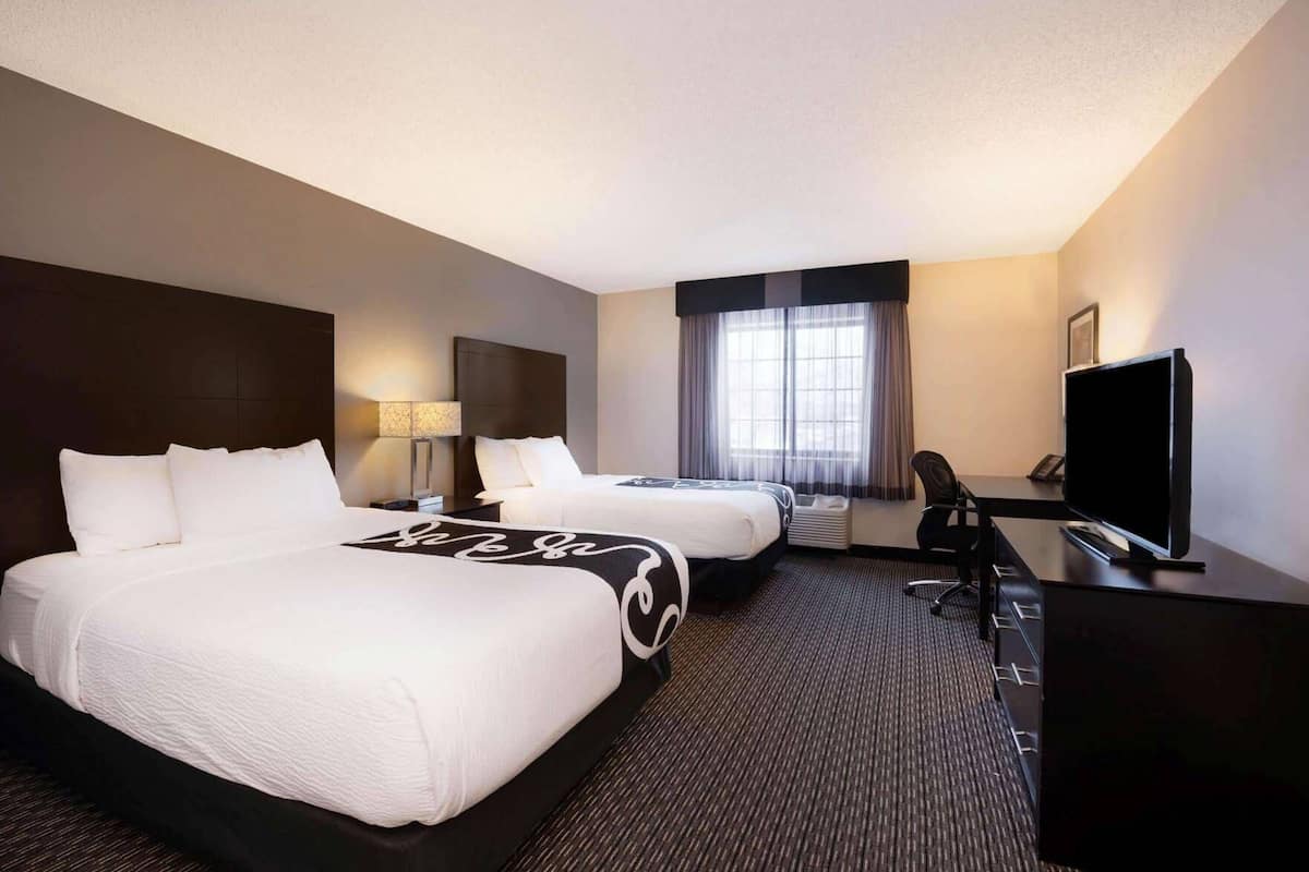 A hotel room with two beds, a desk, a television, and a window with curtains.
