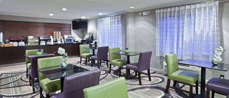 A hotel room with a dining area featuring green and purple chairs, a black table, and a kitchen area with a microwave and coffee maker.