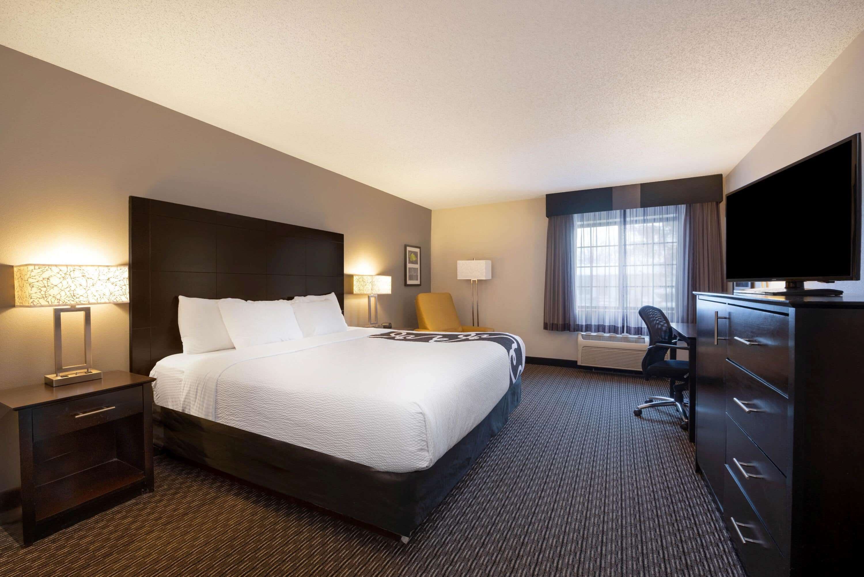 A hotel room with a large bed, a desk, a chair, a television, and a window with curtains.