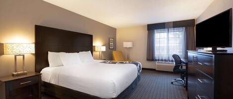 A hotel room with a large bed, a desk, a chair, a television, and a window with curtains.