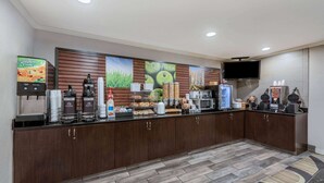 Zona de recepción de un hotel con una máquina de café, un televisor y un mostrador con diferentes alimentos.