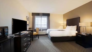 A hotel room with a bed, a desk with a flat-screen TV, a chair, a dresser, and a window with curtains.