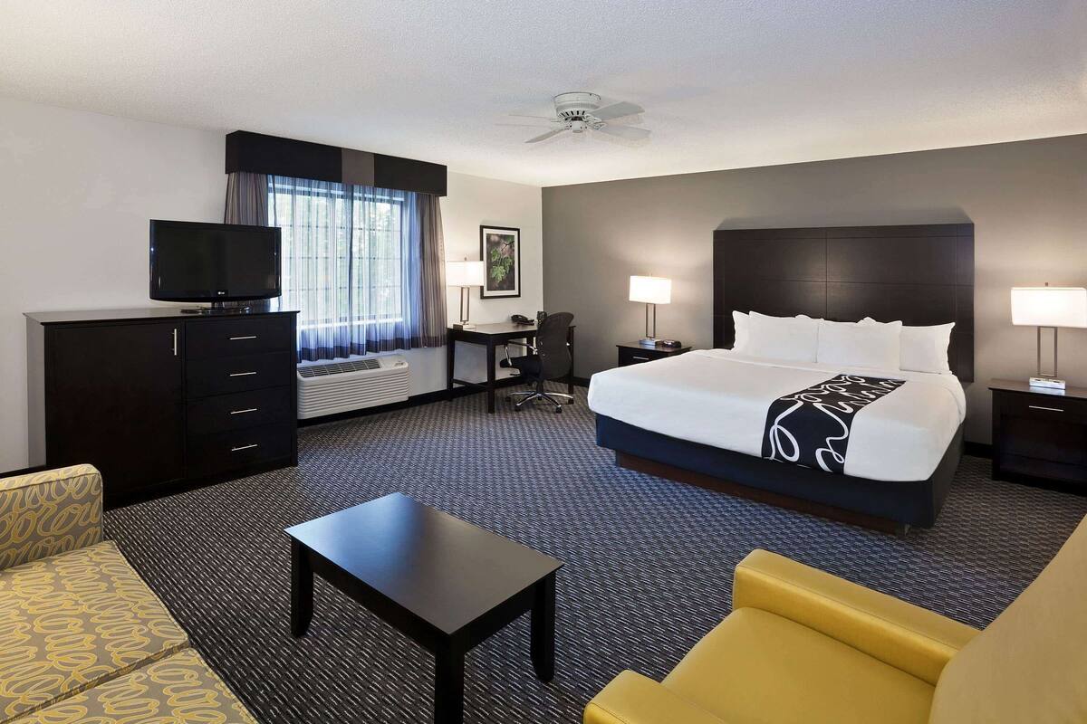 A hotel room with a large bed, a desk, a television, and a sofa.
