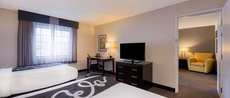 A hotel room with two beds, a desk with a chair, a television, and a yellow armchair.