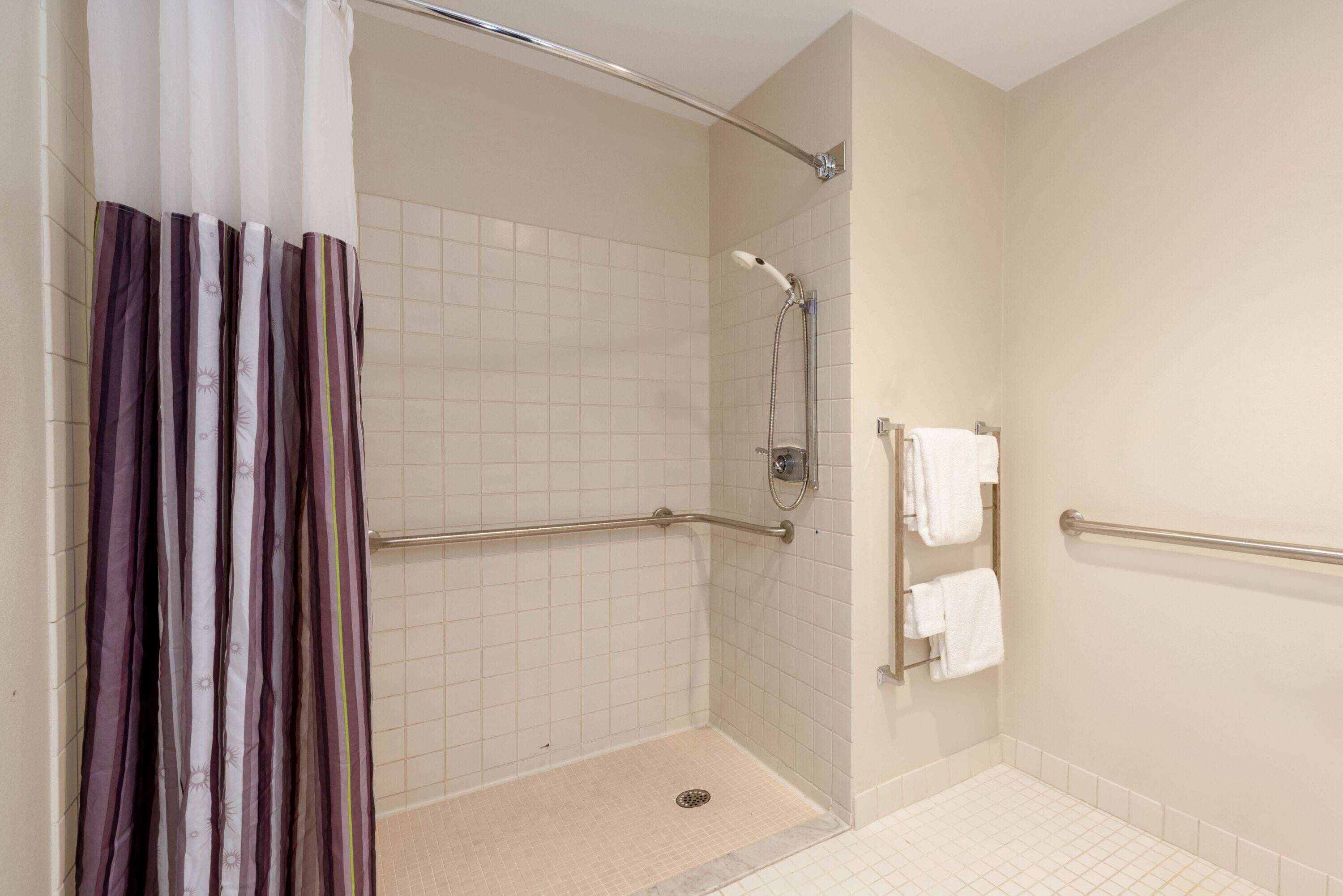 A shower area with a grab bar, a showerhead, and a tiled floor.