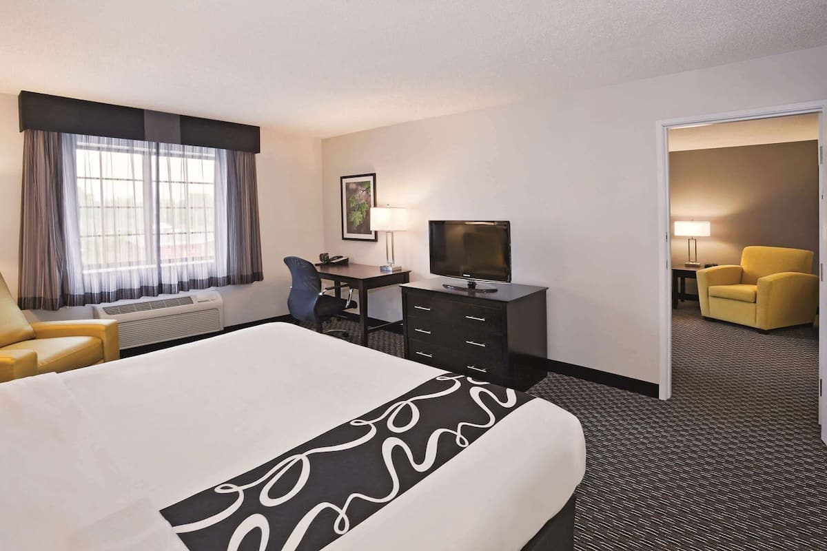 A hotel room with a large bed, a desk with a television, a chair, and a lamp.