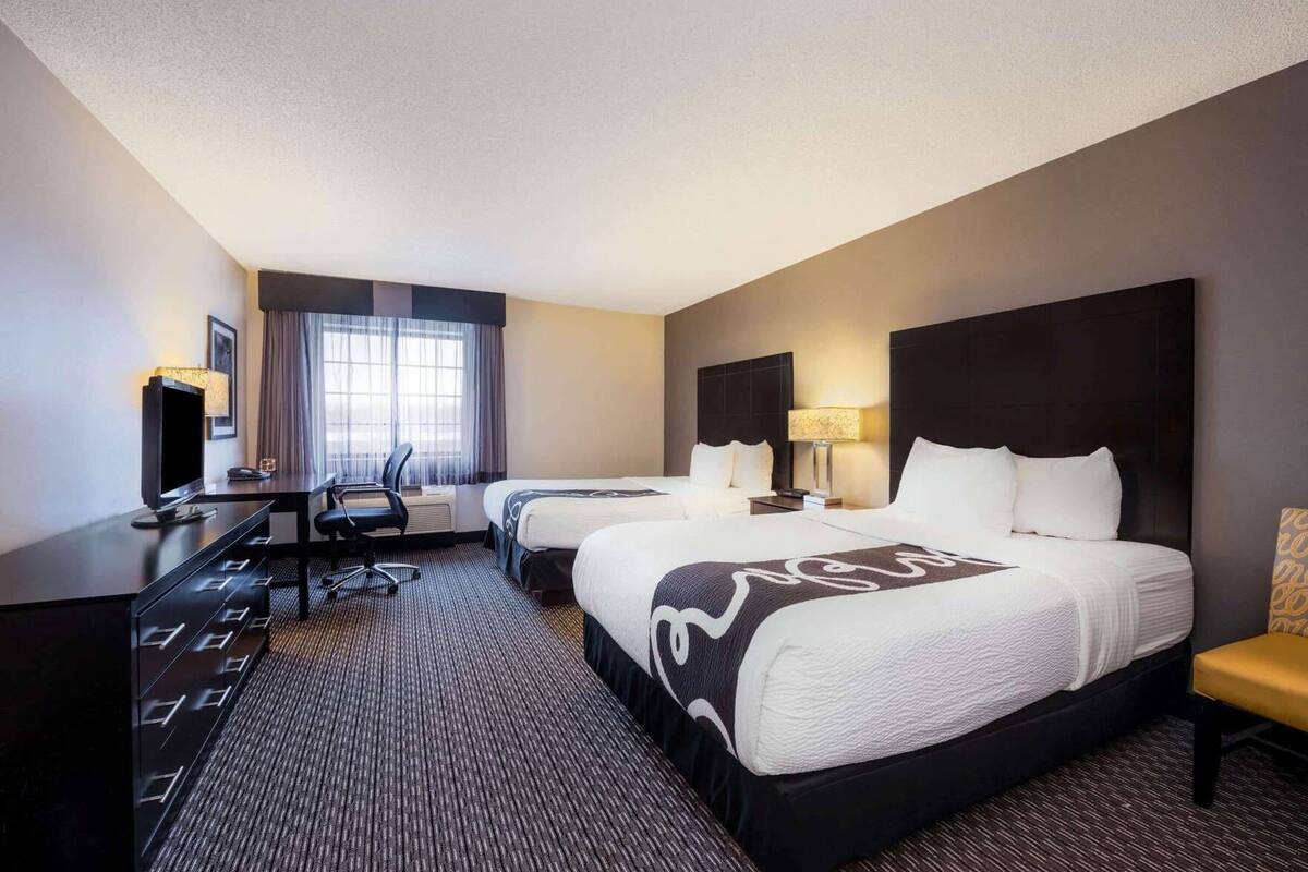 A hotel room with two beds, a desk, a chair, a TV, and a window with curtains.
