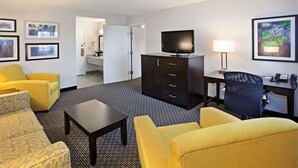 Una habitación de hotel con sofá, sillón, escritorio, televisor y lámpara.
