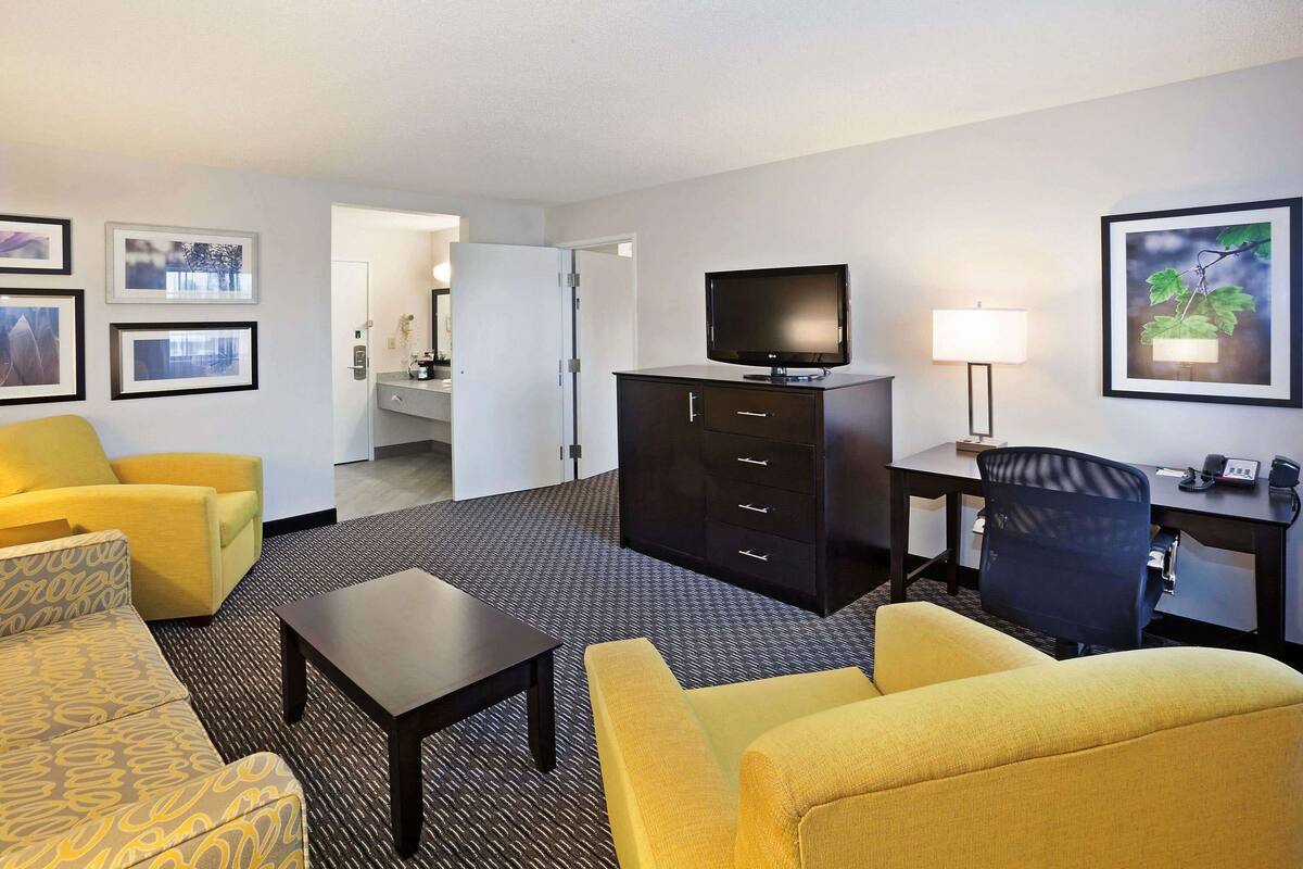 A hotel room with a sofa, armchair, desk, television, and a lamp.
