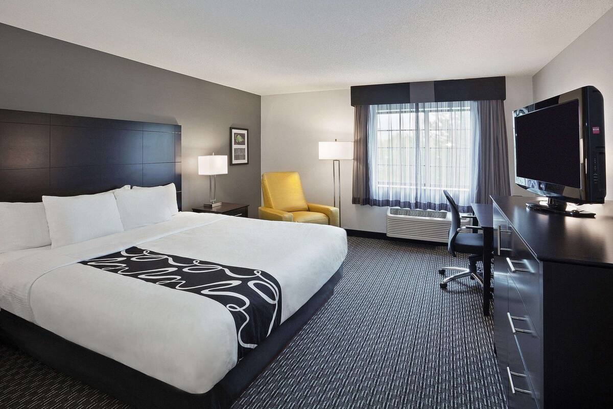 A hotel room with a large bed, a desk with a computer, a TV, and a chair.