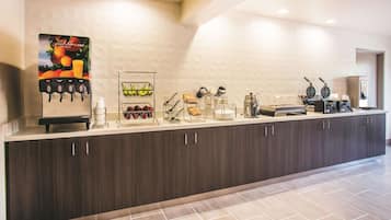 A modern reception area with a juice dispenser, a fruit display, and a coffee machine.