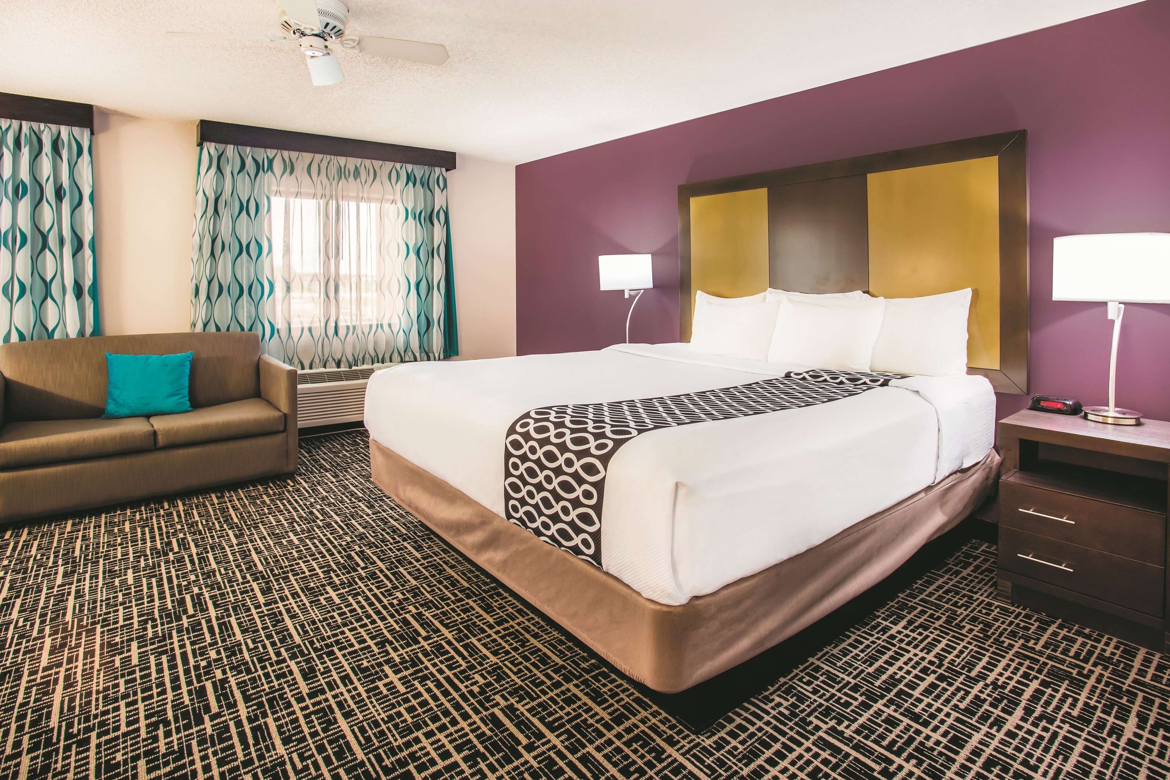 Una habitación de hotel con una cama grande, un sofá, una mesita de noche y un ventilador de techo.
