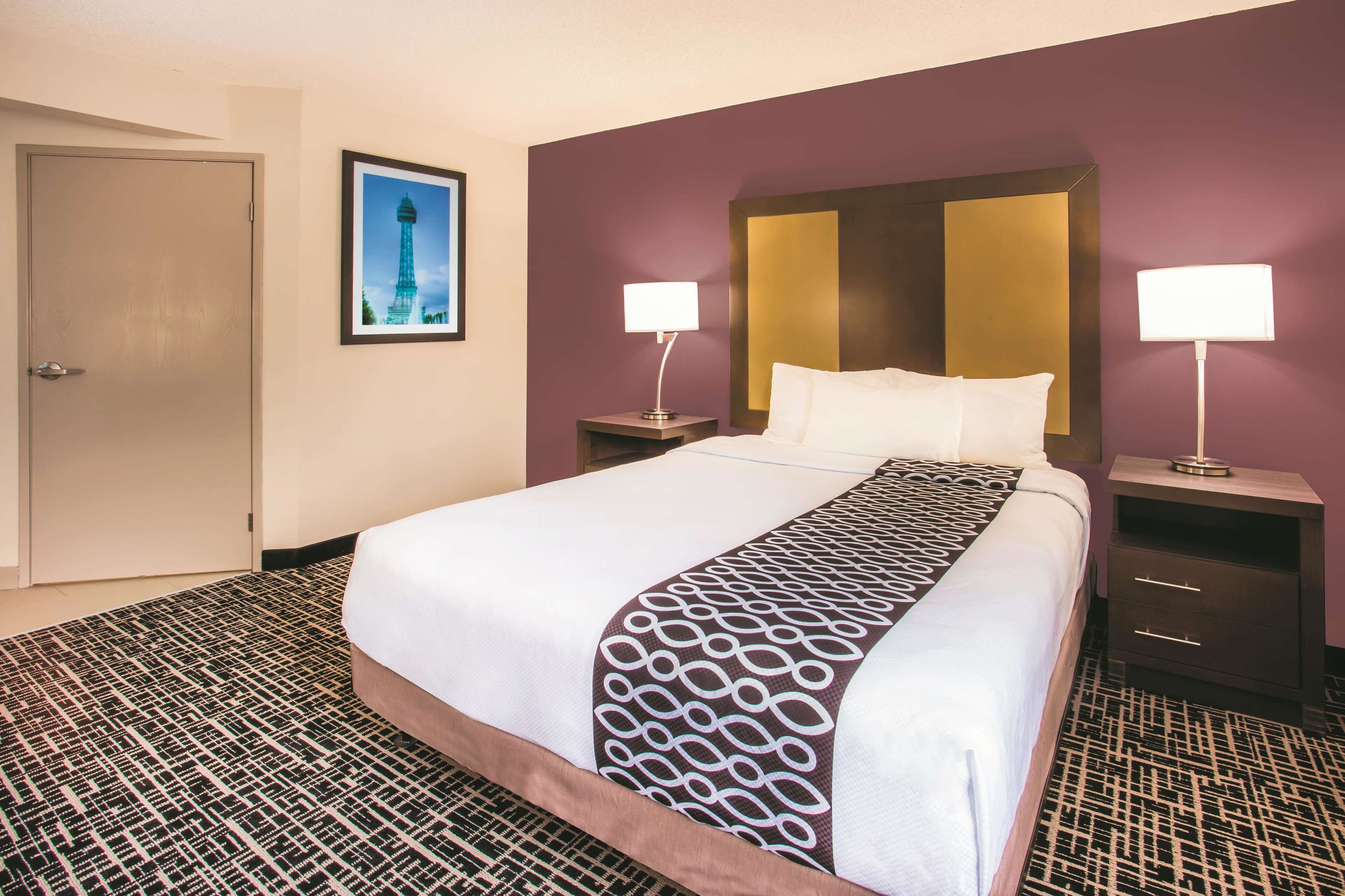 A hotel room with a large bed, two bedside tables with lamps, a door, and a framed picture on the wall.