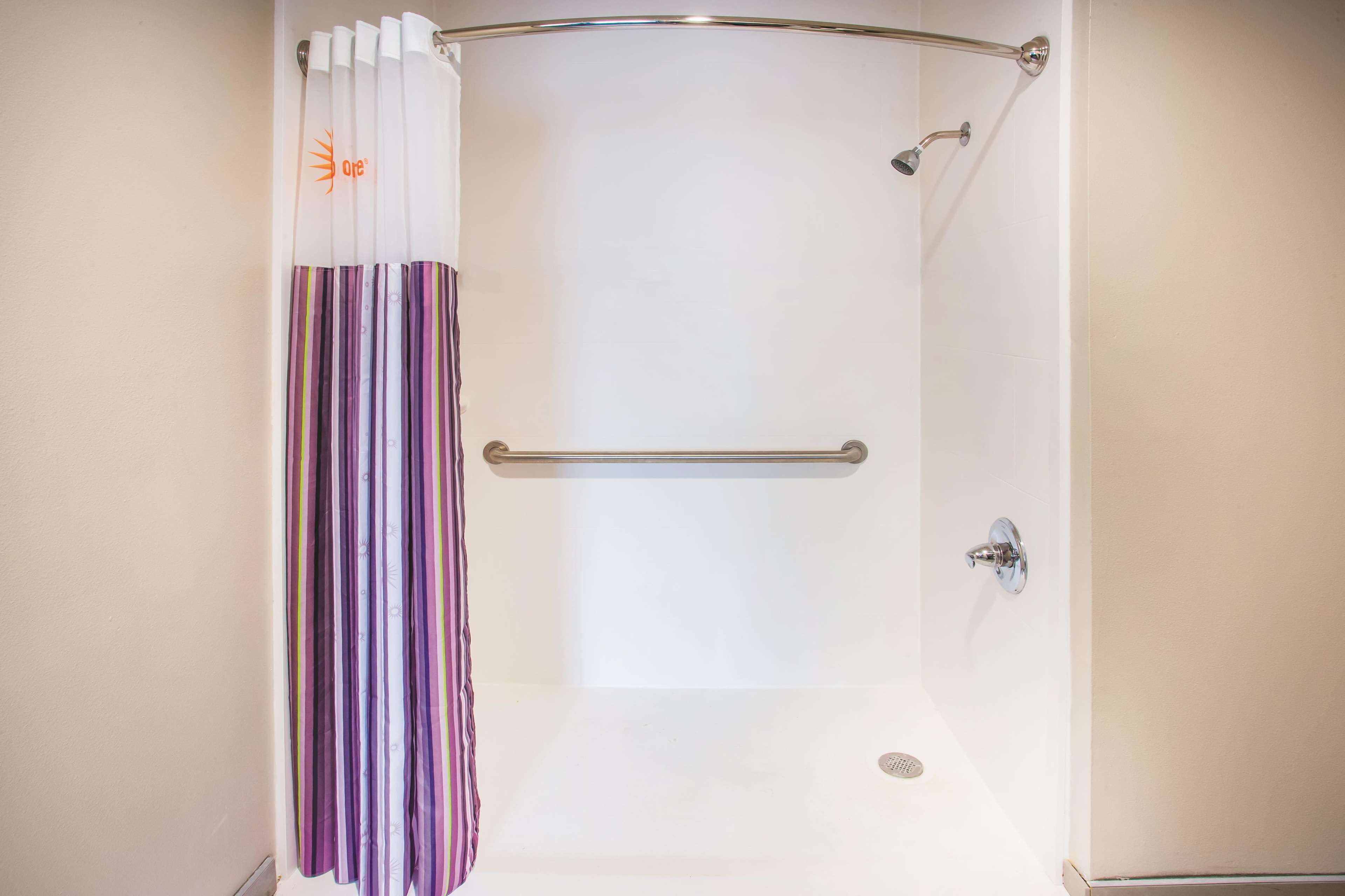 A shower with a white curtain and a metal grab bar.