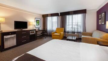 Une chambre d’hôtel avec un grand lit, un bureau avec une chaise, une télévision, un minibar et un canapé.