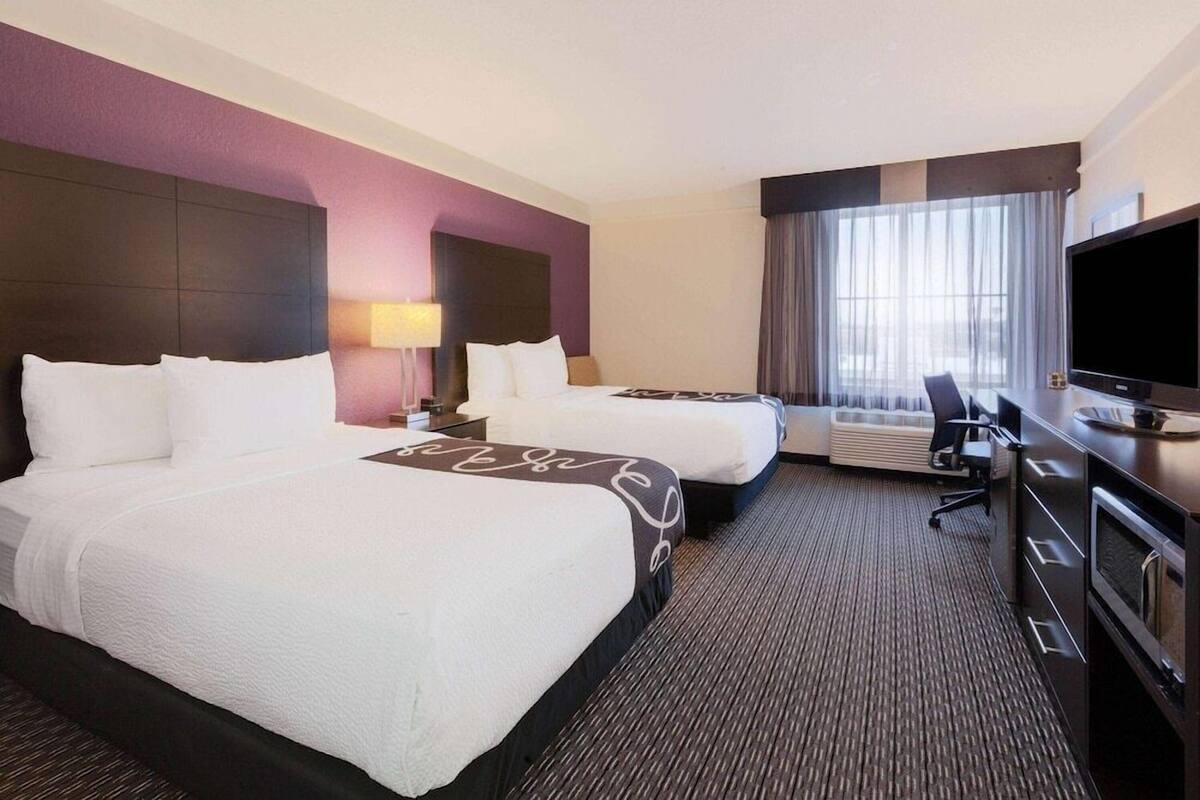 A hotel room with two beds, a desk with a TV, a chair, and a window with curtains.