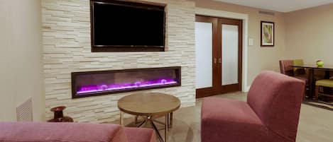 Una sala de estar moderna con un televisor de pantalla plana montado en una pared texturizada, una chimenea empotrada, una mesa redonda de madera y un sofá rojo.