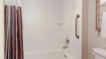 A bathroom with a bathtub, a shower, a toilet, and a handrail.