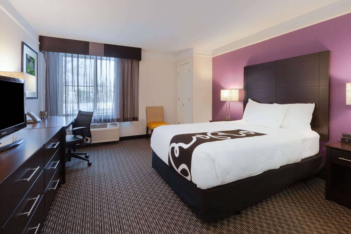 A hotel room with a large bed, a desk with a chair, a TV, and a window with curtains.