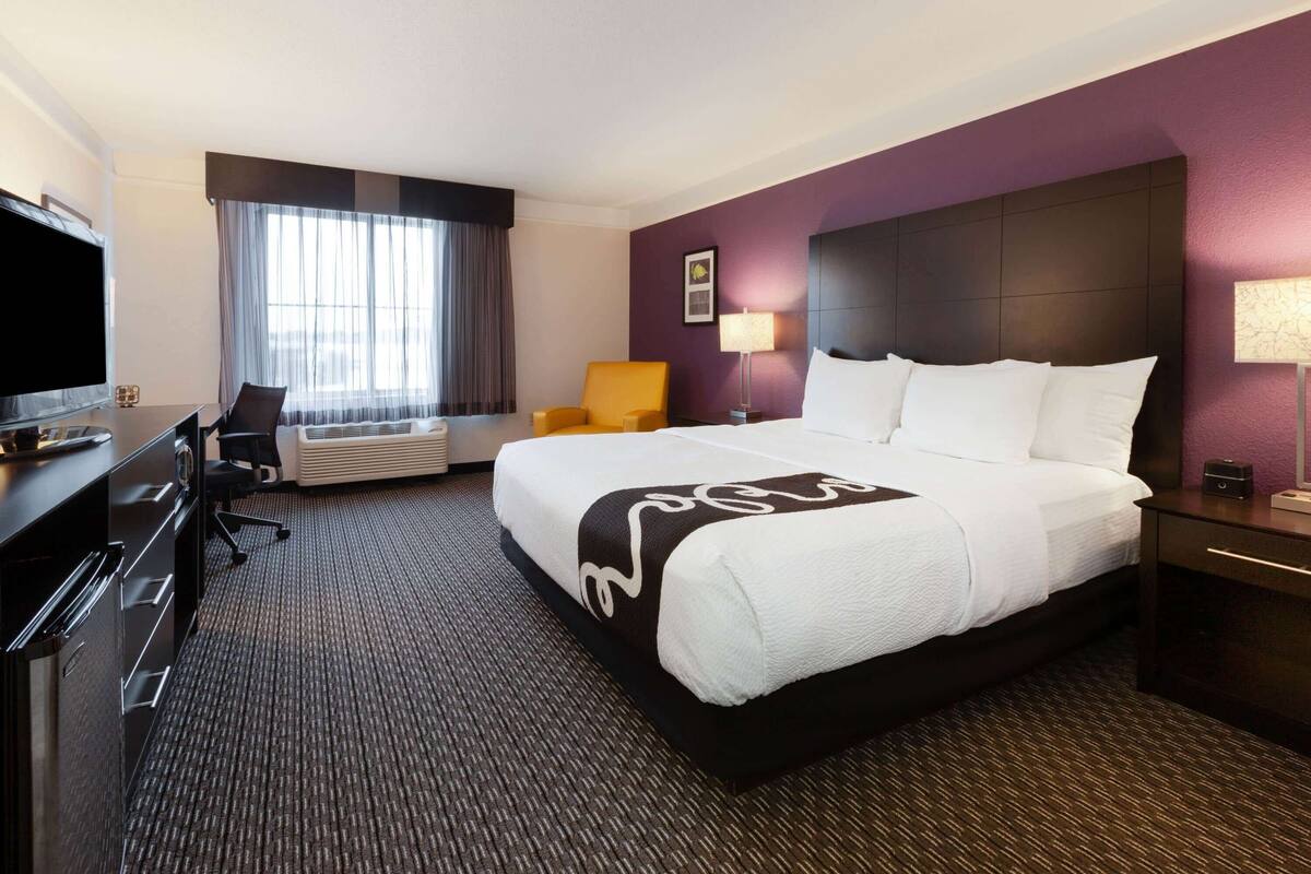 A hotel room with a large bed, a desk with a TV, a chair, and a window with curtains.