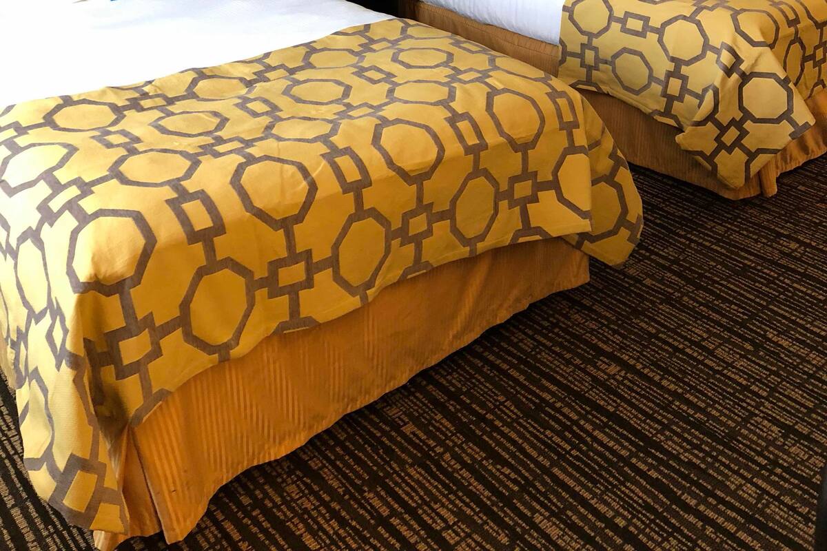 Ein Hotelzimmer mit zwei Betten, einem Nachttisch, einer Lampe und einem gerahmten Bild an der Wand.