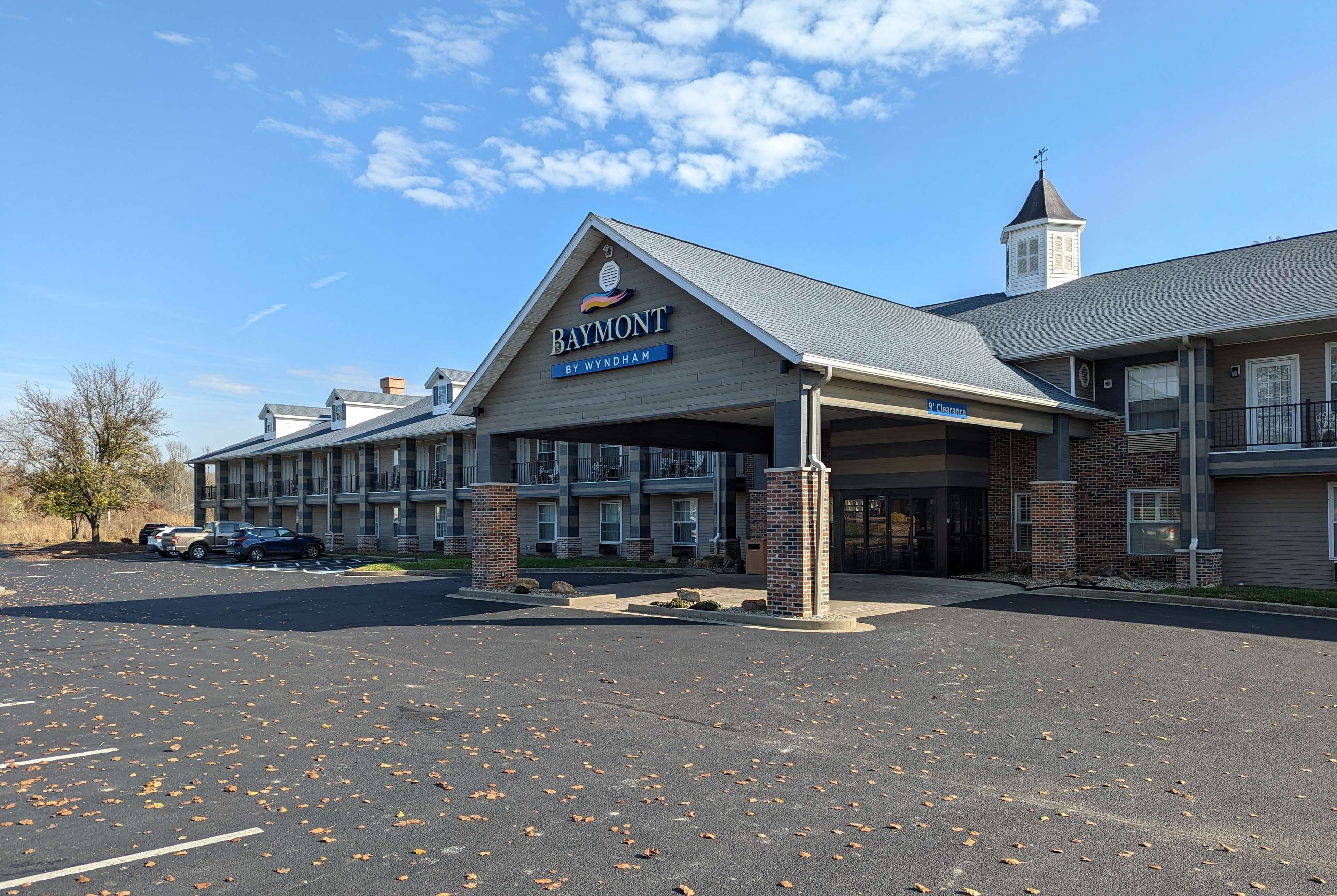 A hotel named Baymont by Wyndham with a covered entrance, brick pillars, and a parking lot with fallen leaves.
