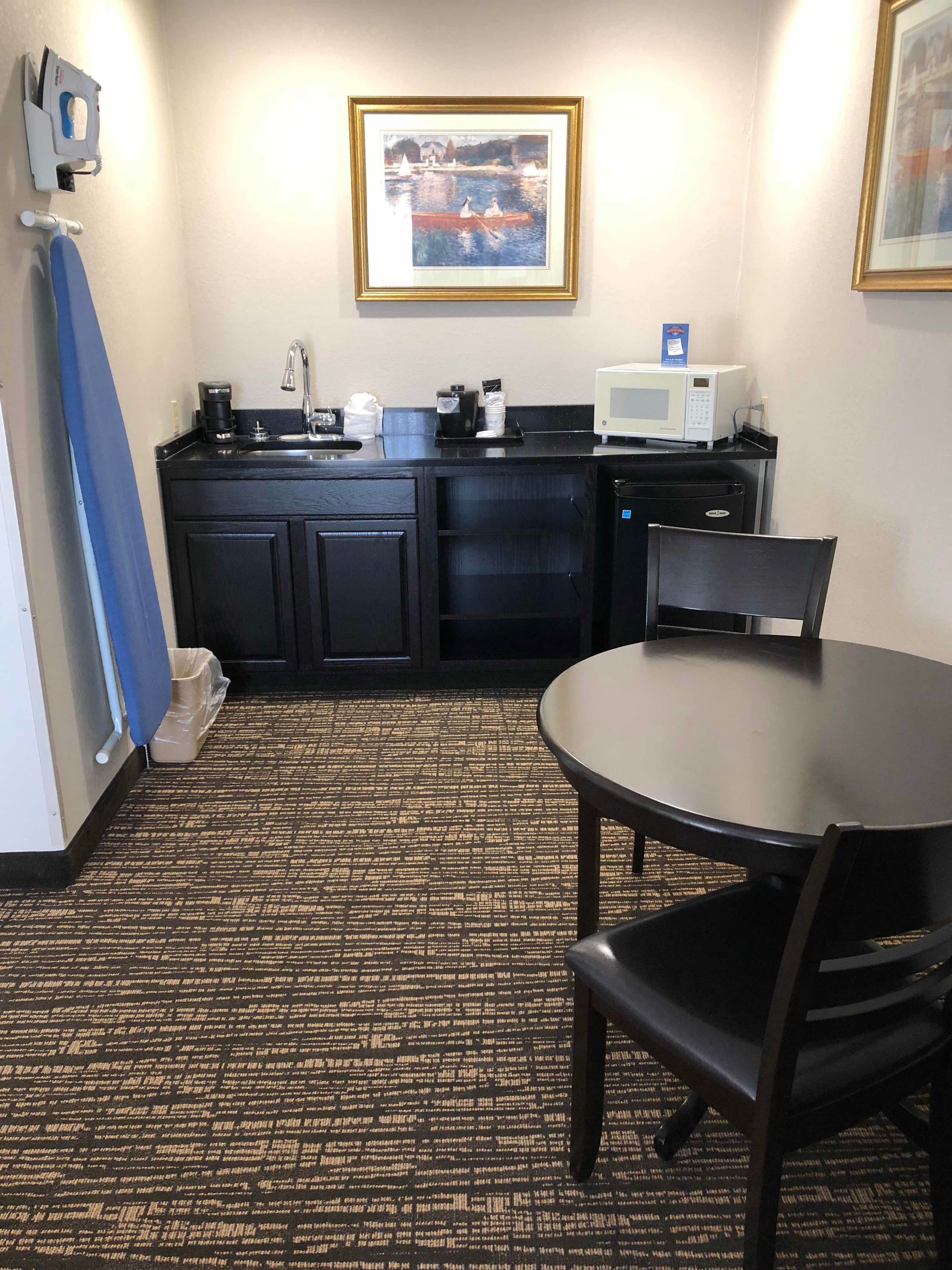 A small kitchenette with a microwave, coffee maker, and sink. There is a framed picture on the wall above the counter.