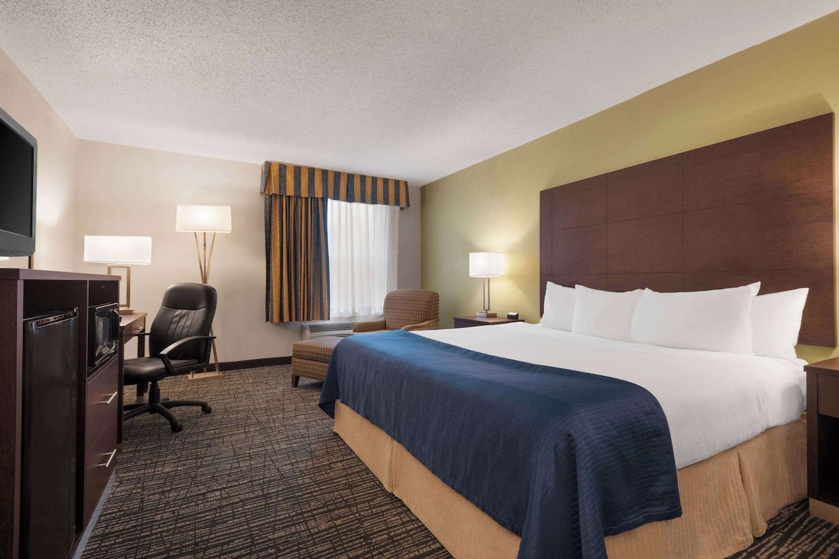 Ein Hotelzimmer mit einem großen Bett, einem Schreibtisch mit Computer, einem Sessel und einem Fernseher.