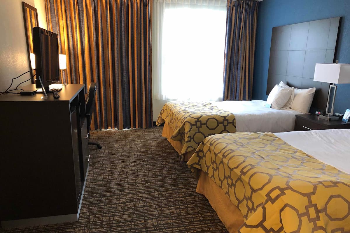 Ein Hotelzimmer mit zwei Betten, einem Schreibtisch mit Computer und einem Fernseher.