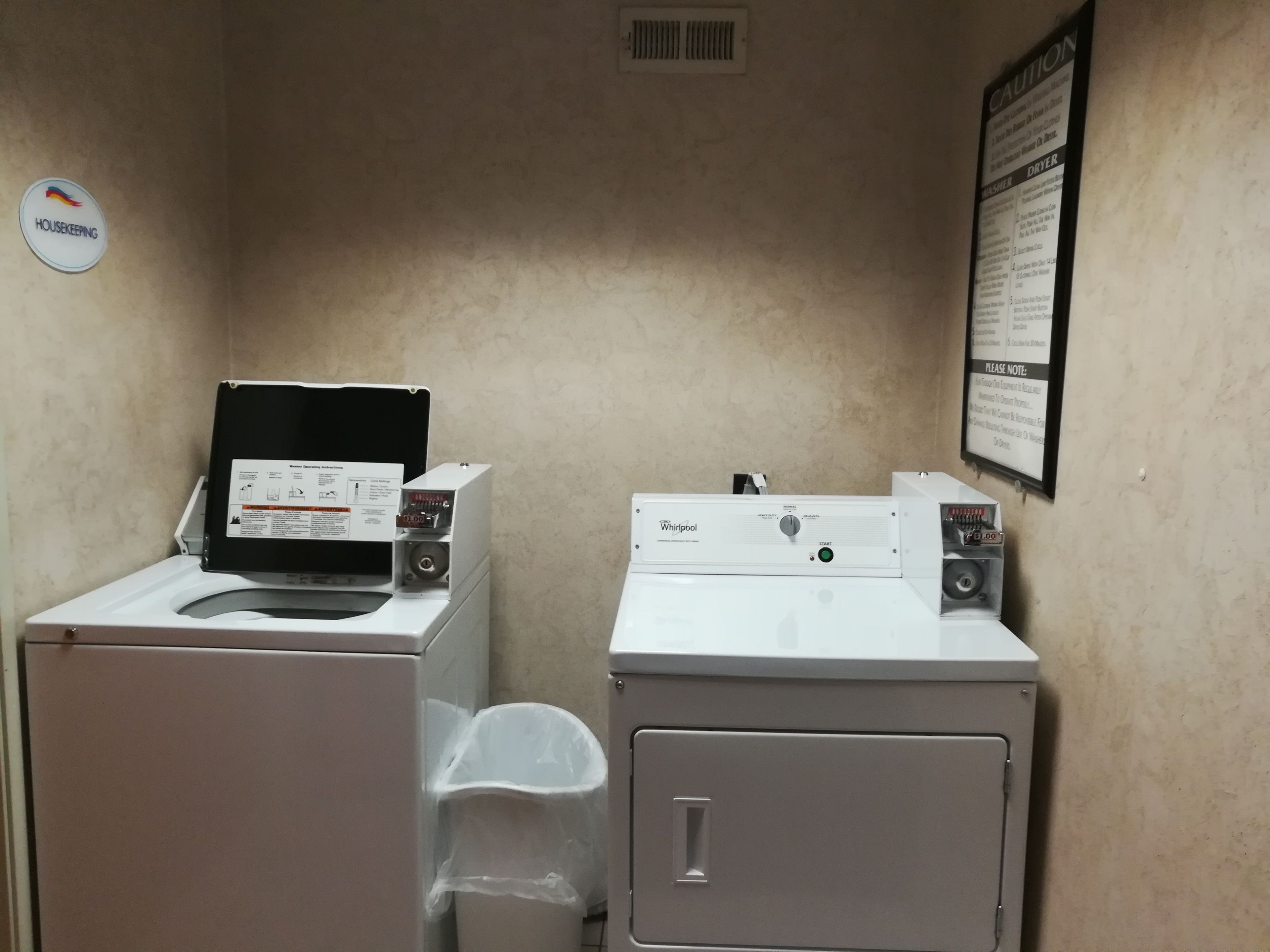 A laundry area with two Whirlpool washers, a dryer, and a trash bin.