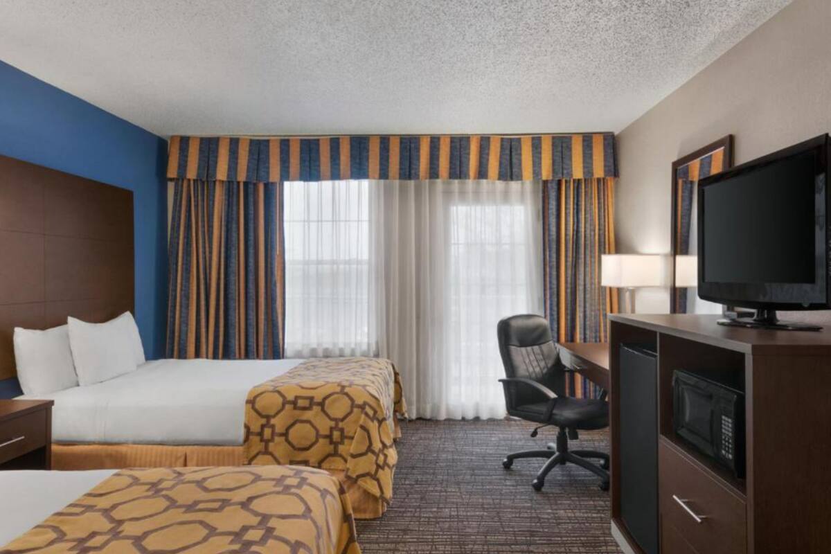 Ein Hotelzimmer mit zwei Betten, einem Schreibtisch, einem Fernseher, einem Sessel und einer Mikrowelle.