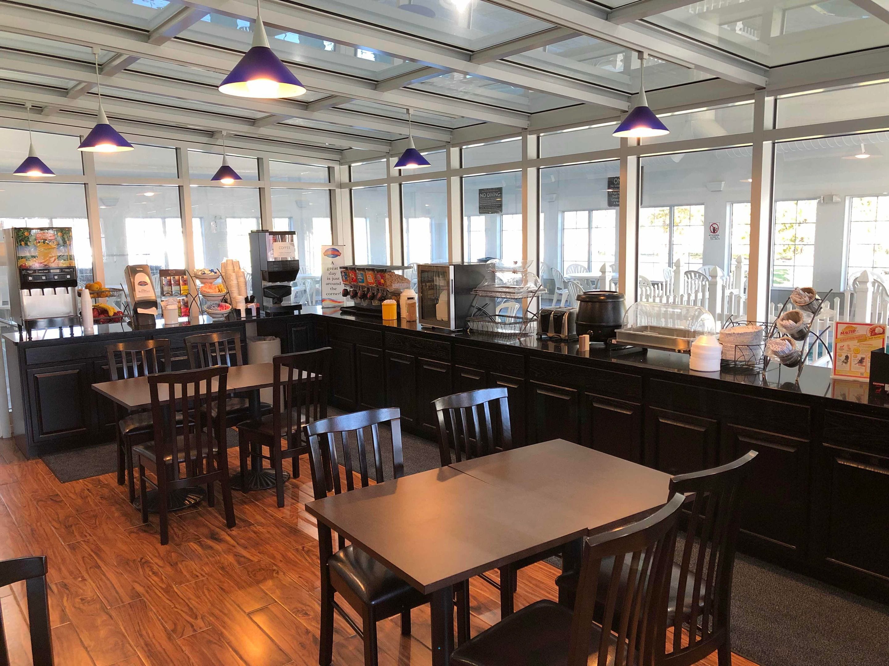 Un restaurante con una decoración moderna, que cuenta con mesas y sillas de madera, una barra de café y grandes ventanales que permiten la entrada de luz natural.