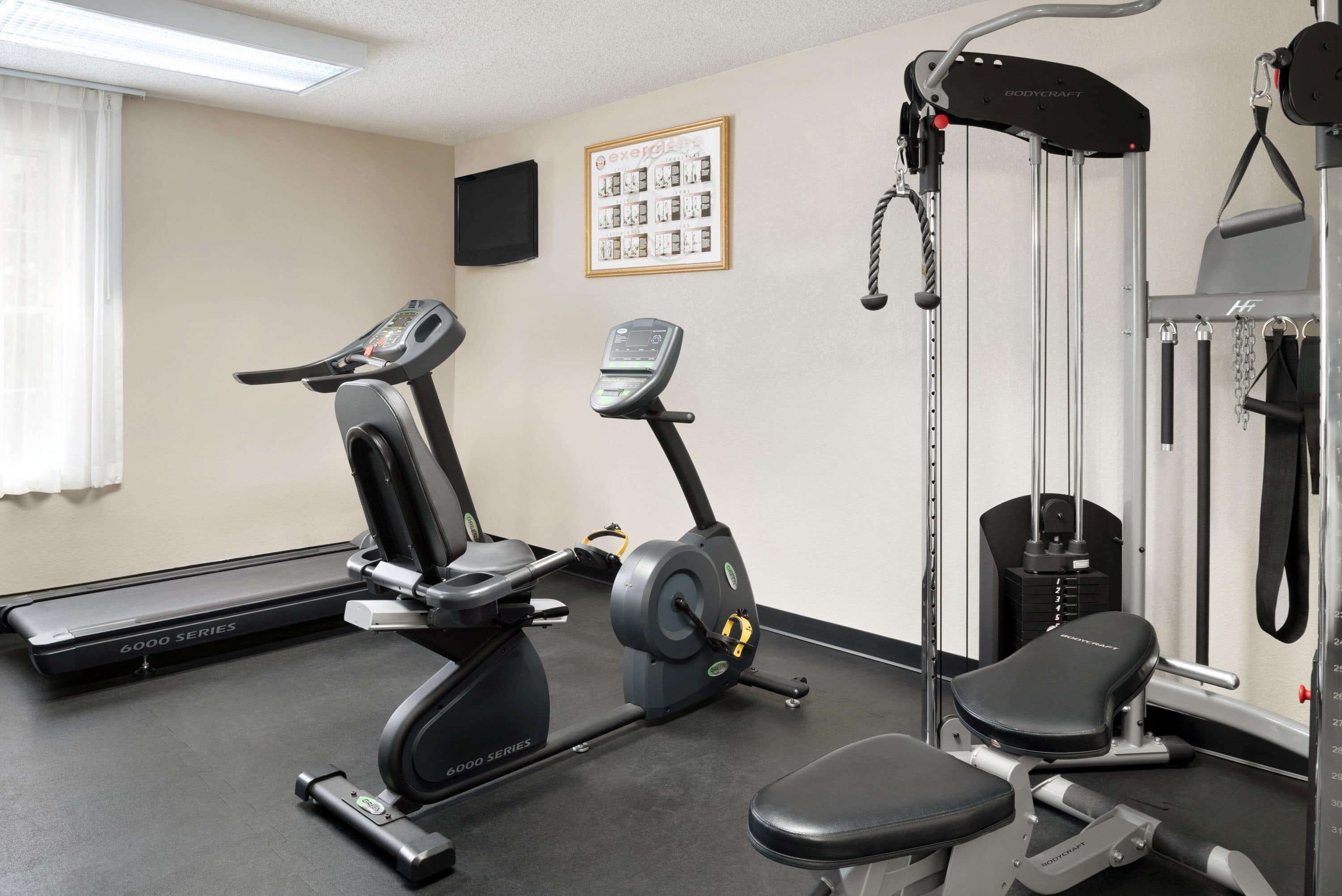Un gimnasio con máquinas de cardio, equipo de levantamiento de pesas y una televisión instalada en la pared.