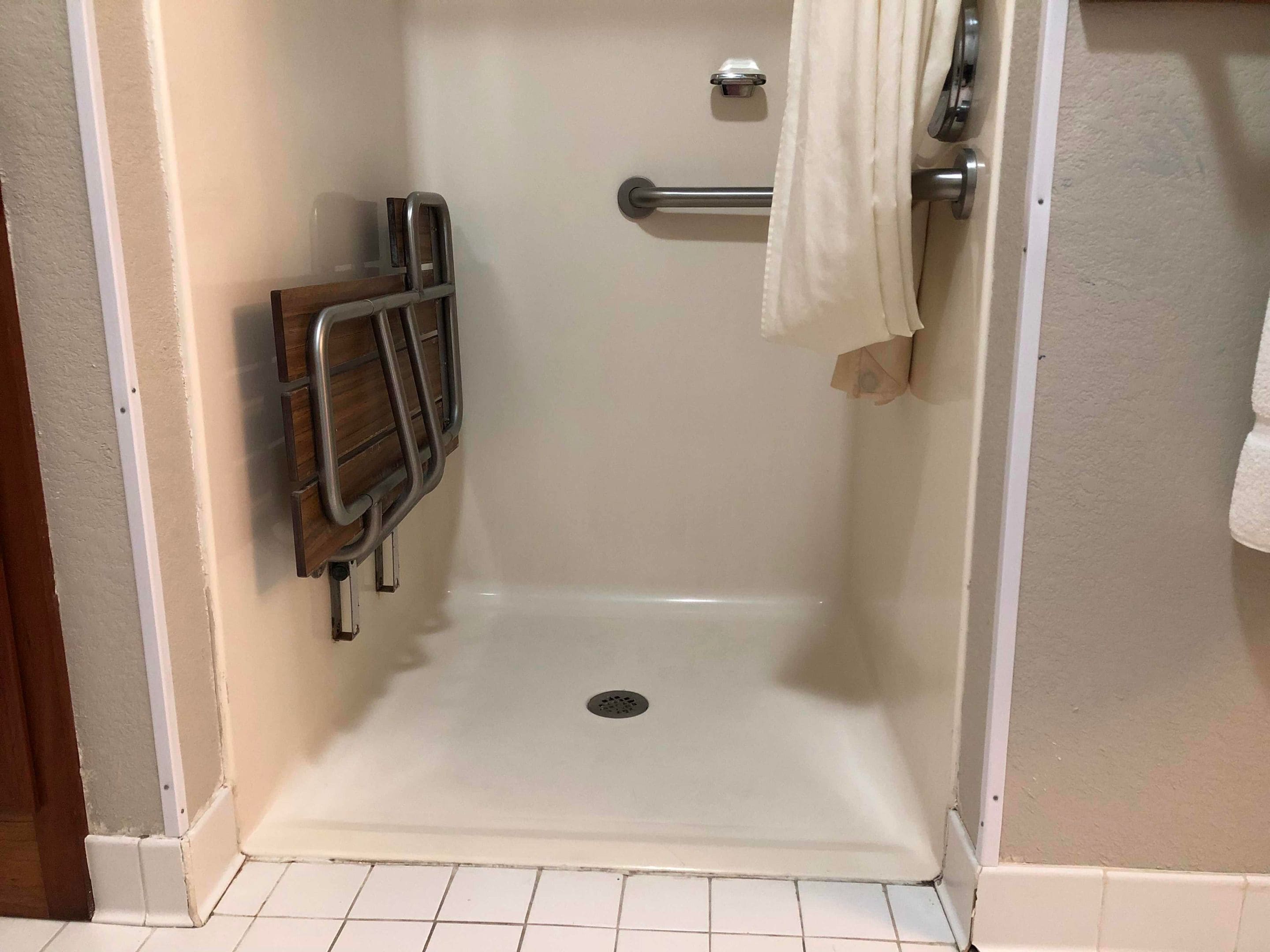 Une douche avec un sol blanc, une barre d’appui en métal et un porte-serviettes.