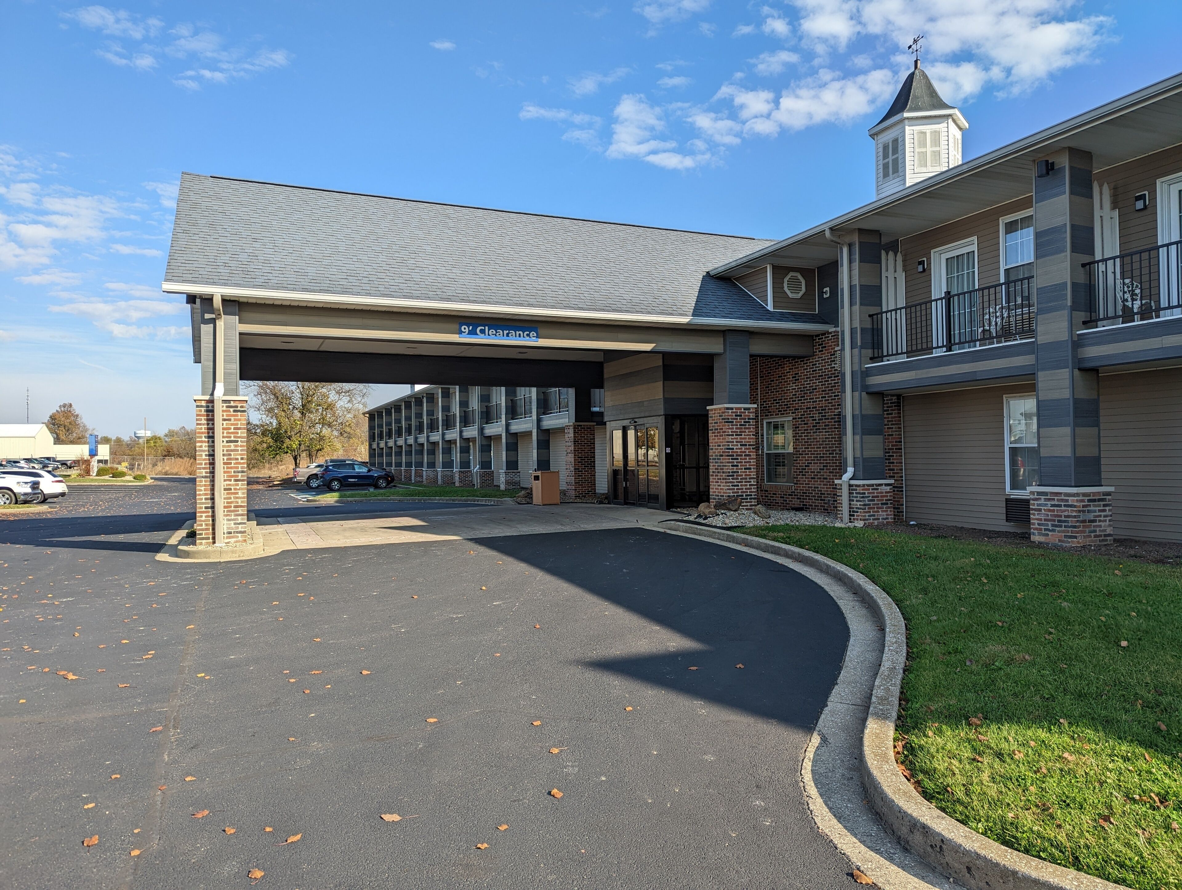 A building with a covered entrance, a sign indicating '9' clearance, and a parking lot with a few cars.