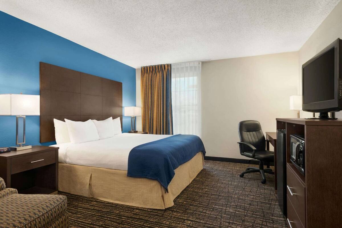 Ein Hotelzimmer mit Bett, Schreibtisch, Sessel, Fernseher und einer Minibar.