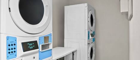 A laundry room with stacked washers and dryers, a control panel, and a table.