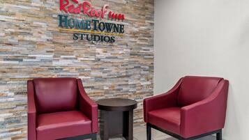 A Red Roof Inn sign on a textured wall, two red chairs, and a small round table.