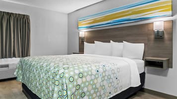 A modern hotel room with a large bed, a headboard with built-in lighting, a bedside table, and a wall-mounted air conditioning unit.