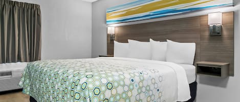 A modern hotel room with a large bed, a headboard with built-in lighting, a bedside table, and a wall-mounted air conditioning unit.