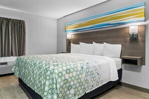 Habitació d'hotel moderna amb un llit gran, un capçal de llit amb il·luminació integrada, una taula de nit i un aire condicionat fixat a la paret.